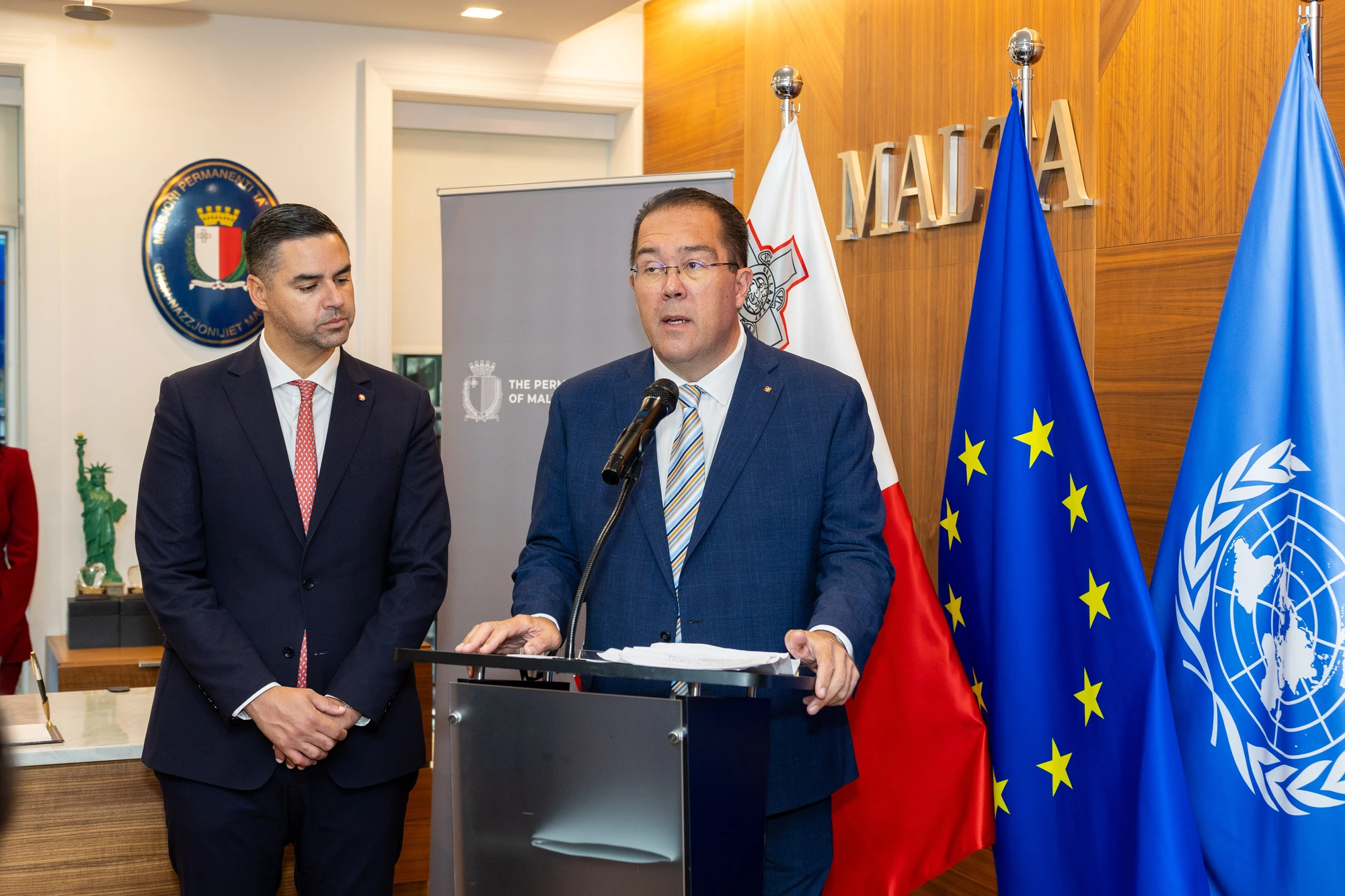 A speaker at a podium beside Malta, European Union and United Nations flags