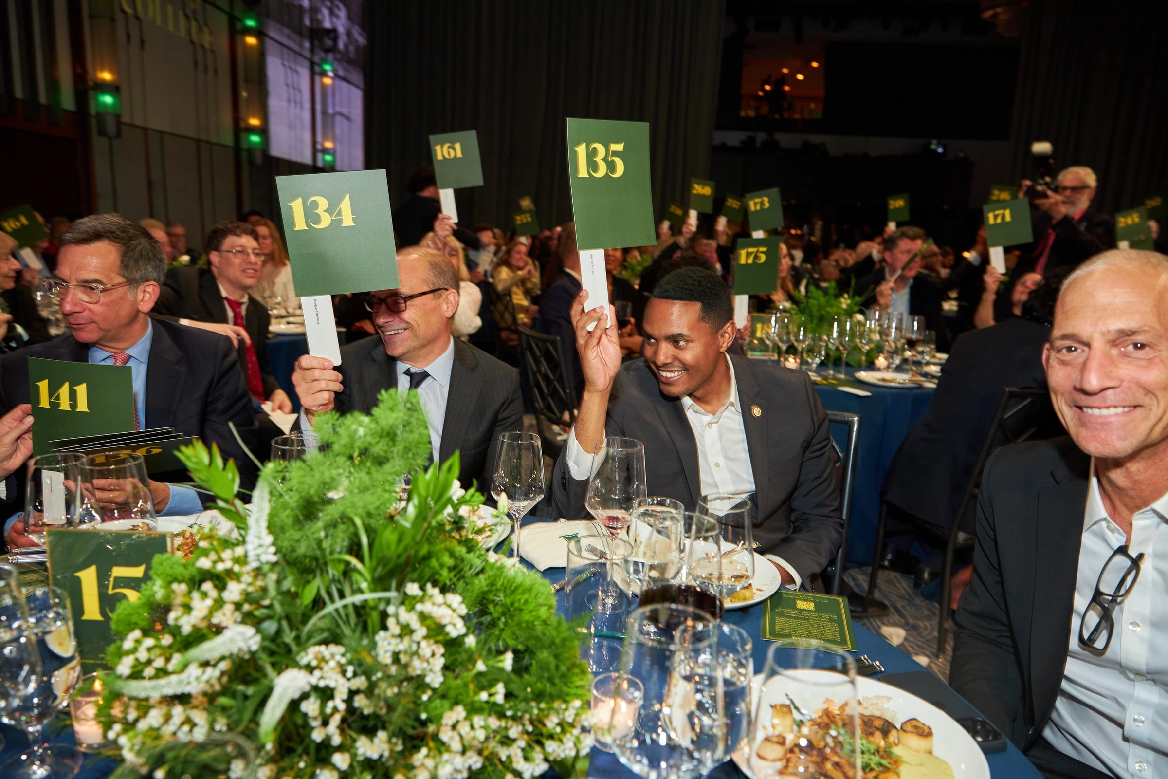 Dinner guests raising auction paddles at a fundraiser